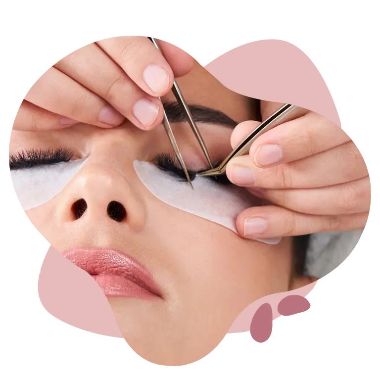 Close-up of a beautician applying eyelash extensions using tweezers on a woman’s closed eye, with protective pads placed under the lashes.